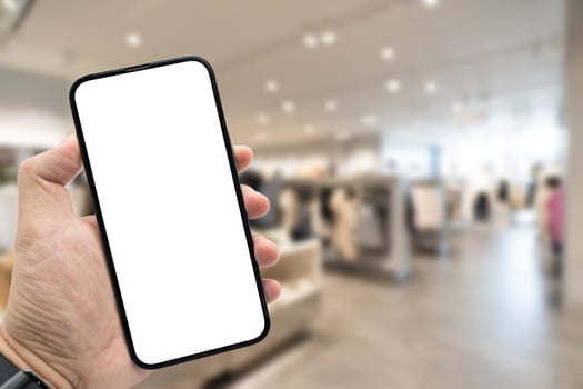 Hand holding blank screen smartphone for copy space on blurred clothing store. e-commerce app shopping mockup. social media, payment and shopping online concept. fashion and technology. photo