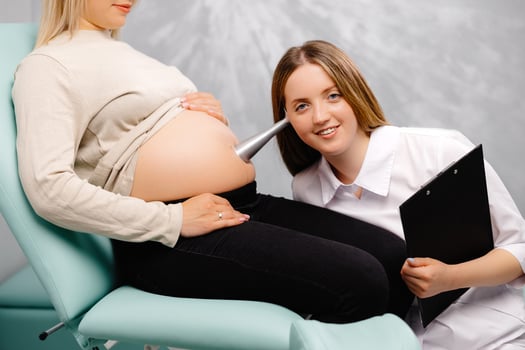 A gynecologist leans a stethoscope to a pregnant woman's belly and listens to the baby's heartbeat photo
