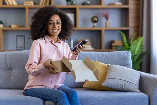 Smiling woman unboxing a package and using her smartphone while relaxing on a couch in a cozy living room. photo