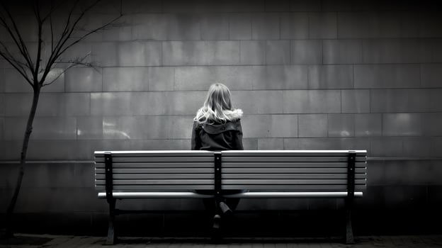 A black and white photo of a woman sitting on a park bench with her hands on her face.
