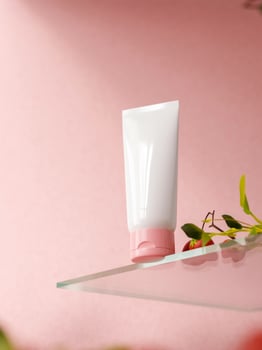 A white and pink tube on a glass pedestal on a pink background. hand cream, or treatment tube mockup photo