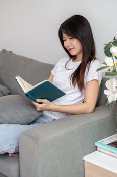 A young, relaxed Asian woman is reading a book on the sofa in the living room at home. photo