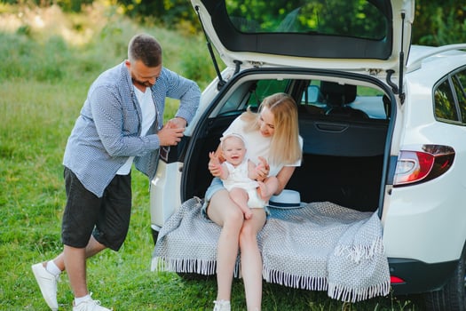 Young family three people in white clothes have picnic. Beautiful parents and daughter travel by car during summer vacation. Scene in park photo