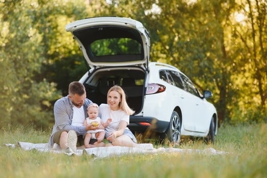 Young family three people in white clothes have picnic. Beautiful parents and daughter travel by car during summer vacation. photo