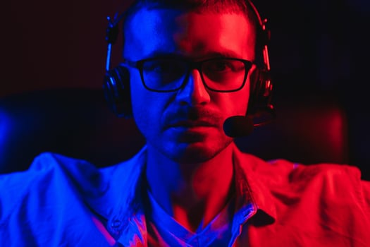 Professional Gamer Plays Game on His Computer. He's Participating in Online Cyber Games Tournament or in Internet Cafe. He Wears Glasses and Talks into Microphone. photo