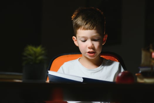 Happy child reading book at table with lamp. photo