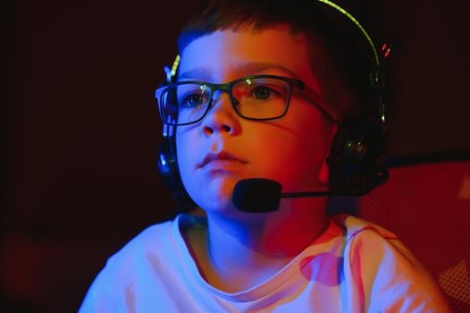 Child online broadcasts computer game, boy streams in headphones on rgb lighting background photo