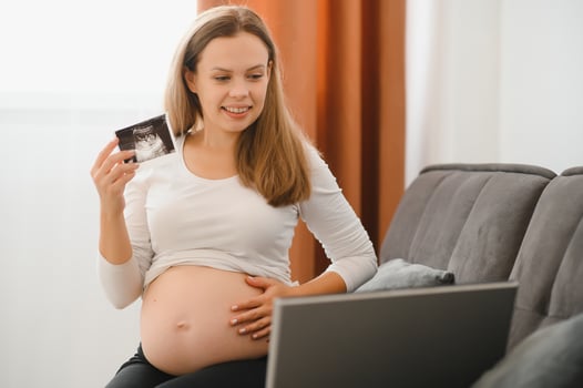 pregnancy, motherhood, people and communication concept - happy pregnant woman with laptop computer having call and showing ultrasound image at home photo