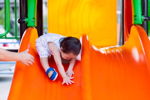 A little boy having fun on a playground slide during a sunny day. Cheerful little boy having fun while sliding outdoors. Parent's hands protecting little child. photo