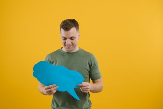Cheerful young male pointing up and holding empty speech bubble with blank space for quote against vivid yellow background photo