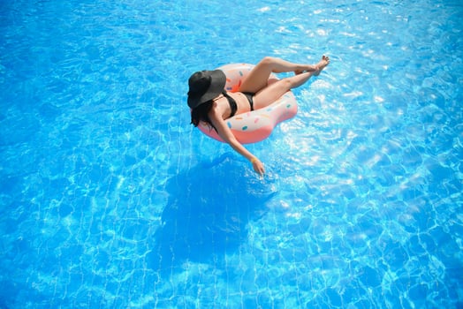 Beautiful young woman with inflatable donut in blue swimming pool photo