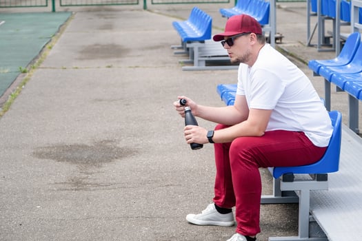sportsman with a bottle of water sitting and resting at the seats at the stadium photo