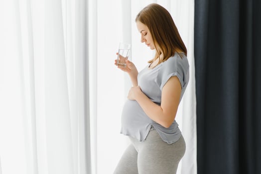 Young pregnant woman standing and drinking water while relax at home. photo