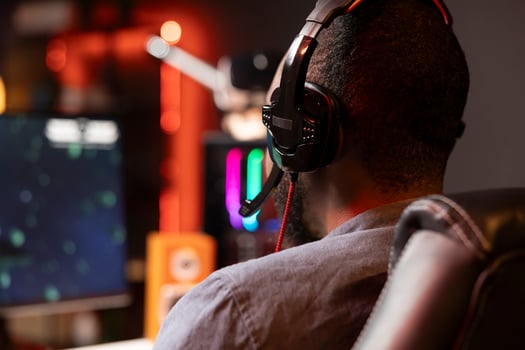 Player using headphones to discuss with mates while playing online videogame on gaming PC monitor. Man enjoying coop game with friends on computer display, chatting on internet late at night photo