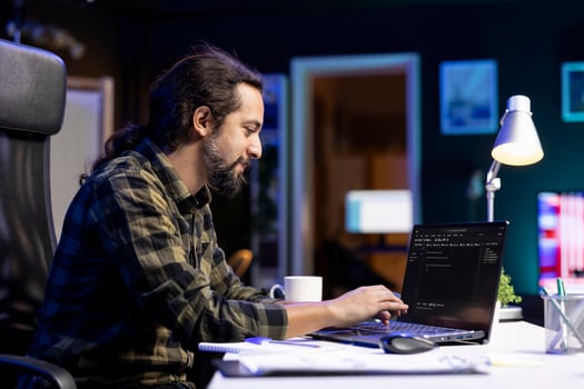 Male programmer works on his portable computer, managing the database and monitoring network for cyber security. Young man sitting at desk and using digital laptop for coding. photo