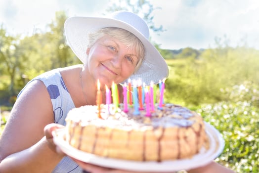 Smiling grandmother holds a birthday homemade cake. Family celebration or a garden party outside in the backyard. photo