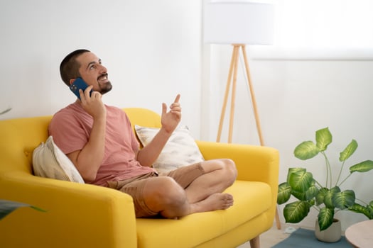 Smiling young man talking smartphone sitting on sofa at home photo