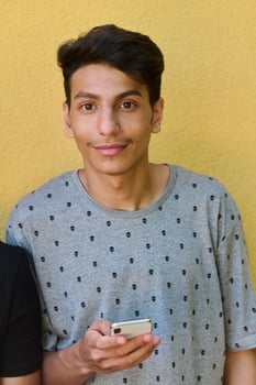Middle Eastern Teenager Using Mobile Phone While Leaning Against Yellow Wall photo