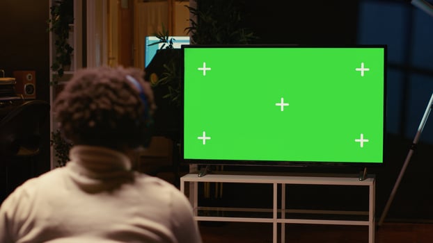 Man playing singleplayer videogames on green screen TV in cozy living room used as home theatre. Gamer using controller to beat game on gaming console attached to mockup television set photo