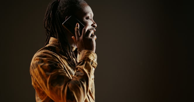 Cool guy with dreads answering phone call in studio, talking to friends or family on camera. African american trendy adult chatting remotely with people on telephone line. Handheld shot. photo