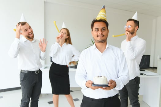 happy business team with birthday cake and gifts greeting indian male colleague at office party photo