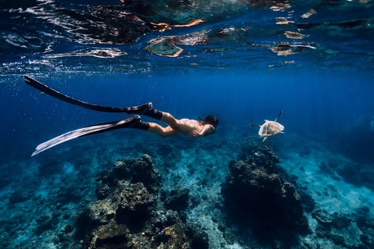Freediver with fins glides underwater with turtle in ocean. photo