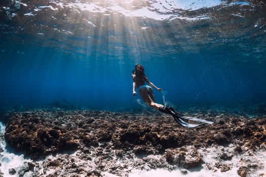 Woman freediver with fins glides underwater in blue ocean. Freediving or swimming in sea photo