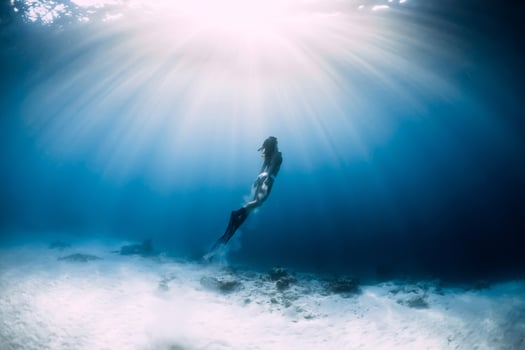 Freediver woman with fins glides over sandy sea bottom in sea. Freediver and amazing light photo