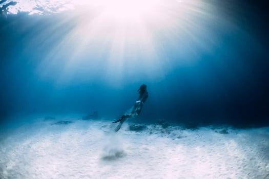 Free diver girl with fins glides over sandy sea in ocean. Freediver and amazing light photo