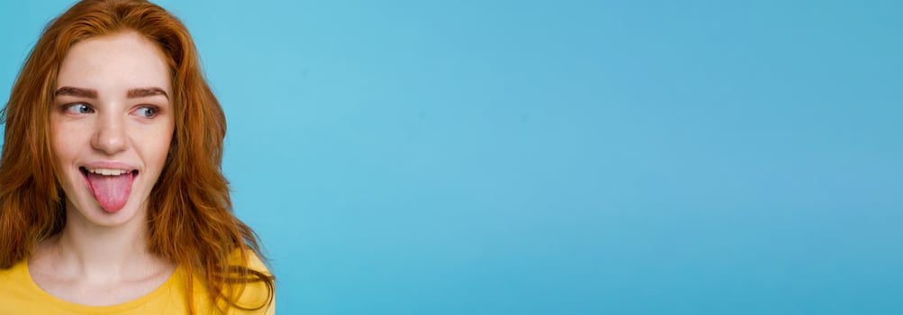 Headshot Portrait of happy ginger red hair girl with funny face looking at camera. Pastel blue background. Copy Space photo