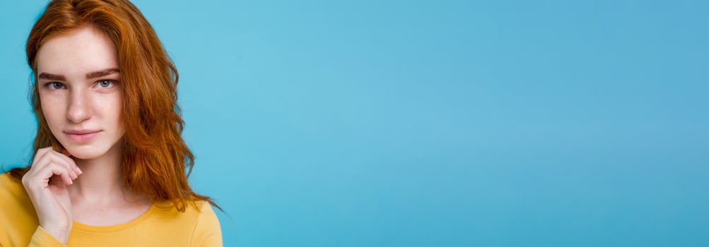 Headshot Portrait of happy ginger red hair girl with freckles smiling looking at camera. Pastel blue background. Copy Space photo