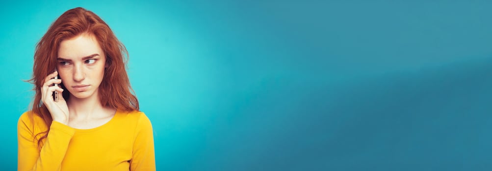 Lifestyle concept - Portrait of ginger red hair girl with shocking and stressful expression while talking with friend by mobile phone. Isolated on Blue Pastel Background. Copy space photo