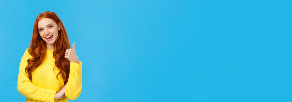 Wonderful idea. Supportive cute redhead girlfriend encourage you try, approve good choice, smiling pleased, nod approval and showing thumb-up like gesture, stand blue background photo