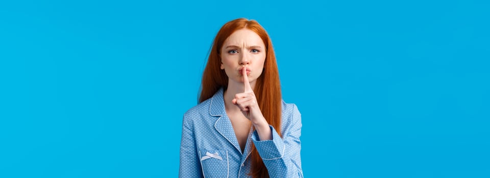 Quiet please Im trying sleep. Displeased and disturbed young redhead college girl living dormitory asking roommate be silent, shushing, say hush angry frowning, press index finger to lips photo
