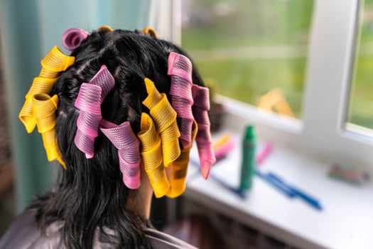 A woman with long black hair gets her hair styled with pink and yellow curlers photo