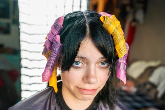 A young woman with black hair is getting her hair styled with purple and yellow rollers photo