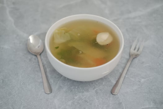 A bowl of soup with a spoon and fork on a wooden table photo