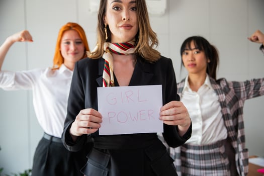 Businesswoman holds a paper with Girl Power written on it while her colleagues flex their muscles photo