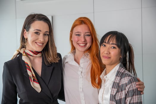 Three young business women smiling together in the office, multi ethnic group photo