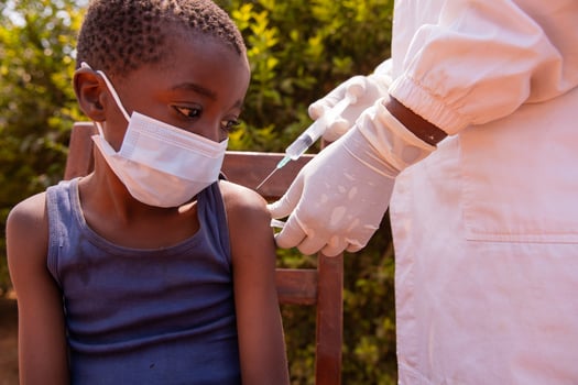 A little child wearing face mask sitting on a chair taking his injection photo