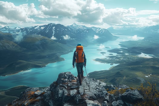 Person with orange backpack on mountain, looking at lake photo