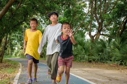 Group of three Asian boys were running fast without care is causing an accident or falling in danger on the road in the park on forest background. photo