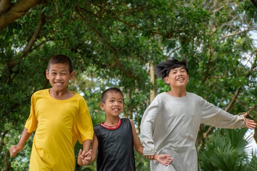 Group of asian children holding hands and running happily joyful at outdoor park in forest spring blurred background. Asian kids playing in the garden summer holiday. photo