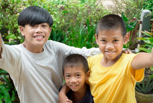 Group of Asian young boys friends taking selfie picture smiling charming and looking at the camera phone against outdoor green forest background for concept of multicultural people having fun day. photo