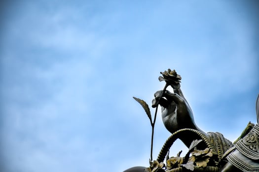 Part of a hand holding a lotus is a statue of a Chinese god a sculpture made of black iron in a Chinese shrine on a sky background. photo
