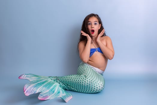 Shocked girl in mermaid costume sitting on blue background photo