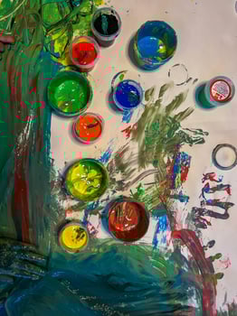 Little cute child with a brush and a palette of paints in his hands draws on a white wall. Happy childhood photo
