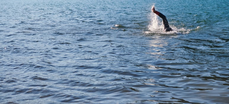 Triathlon athlete swimming on lake in sunrise wearing wetsuit photo