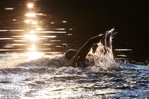 Triathlon athlete swimming on lake in sunrise wearing wetsuit photo
