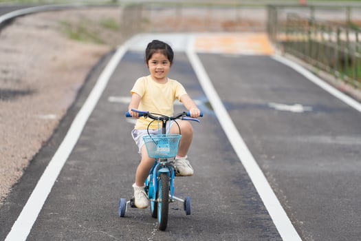 Asian baby girl child smiling and learning to ride bicycle in the park garden. Education concept for kid practiice cycling at park, baby sport concept. photo
